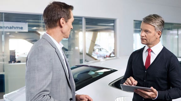En man och en Audi servicepersonal stående mot varandra och pratar i en audiverkstad