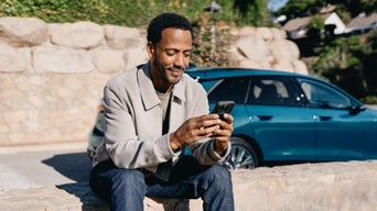 Ein Mann schaut auf sein Handy und sitzt neben einem blauen Audi Modell.