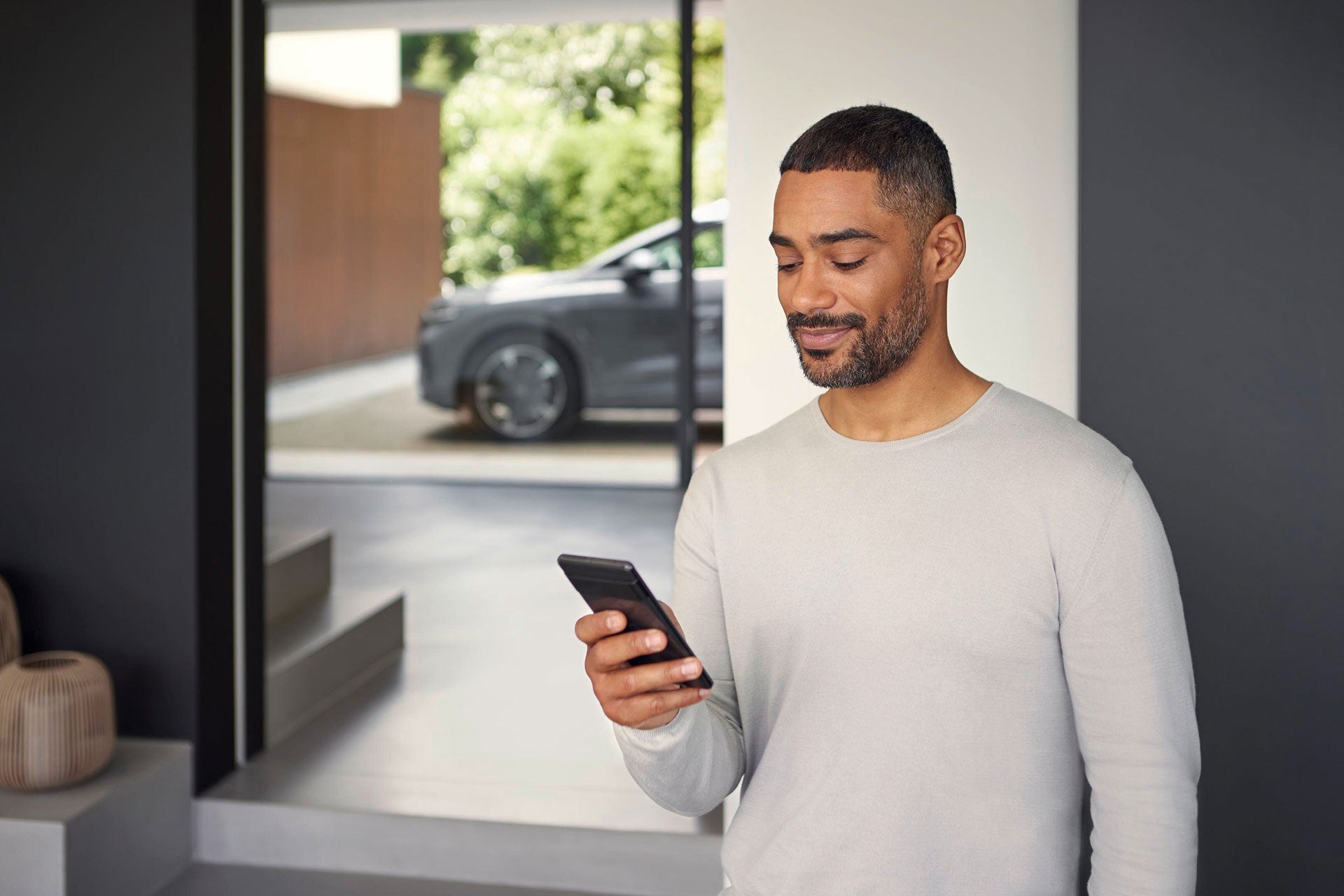 Ein Mann schaut auf ein Handy im Hintergrund die Front eines grauen Audis