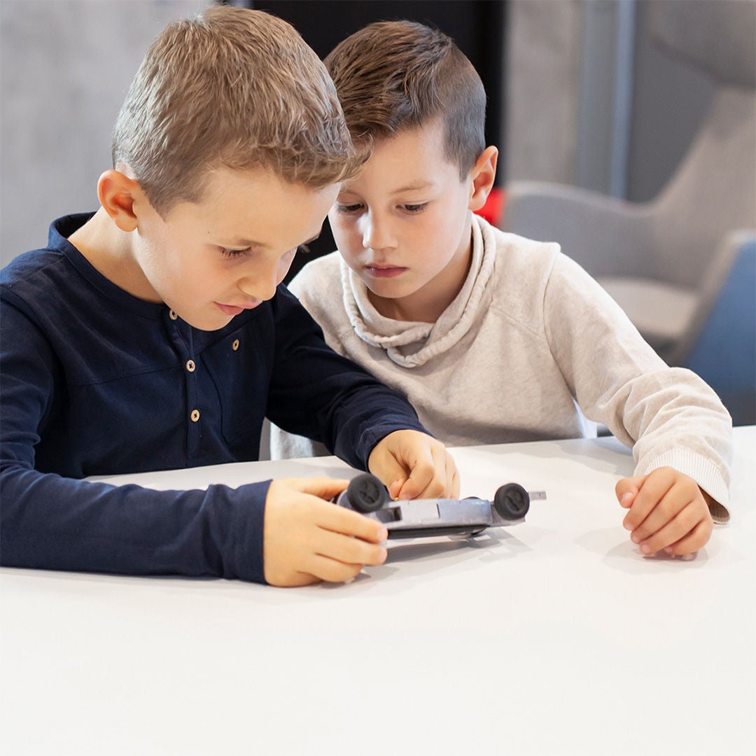 Zwei Jungen betrachten an einem Tisch ein kleines Modellauto und halten es gemeinsam in den Händen.