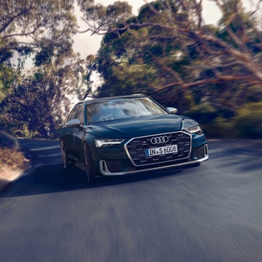 Dunkelblauer Audi S6 Avant TDI fährt auf kurviger Straße durch bewaldete Landschaft, dynamische Bewegung sichtbar.