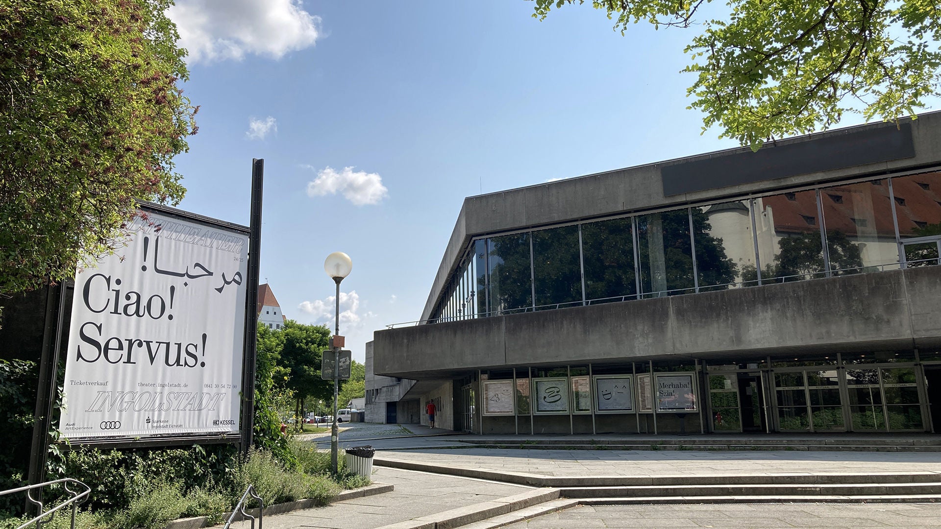 Außenansicht des Stadttheaters Ingolstadt mit großem Plakat 'Ciao! Servus!'.