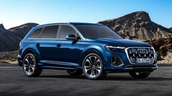 The Q5 SUV in a three-quarter view in a parking lot, with the outline of a futuristic building on the right in the background and the sea on the left.
