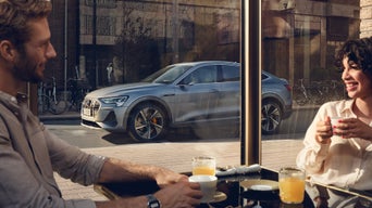 Kvinne og mann på cafe med Audi e-tron Sportback i bakgrunnen.
