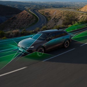 Der Audi A6 allroad schräg von vorne auf einer kurvigen Gebirgsstraße. Das Bild zeigt durch blau und grün markierte Bereiche die Erkennung von Fahrbahnbegrenzungen durch den adaptiven Fahrassistenten.