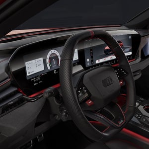 Widok na kokpit Audi RS 5 Avant od strony kierowcy. Widoczne są kierownica, cyfrowe wyświetlacze oraz czerwone światło interakcyjne pod przednią szybą.