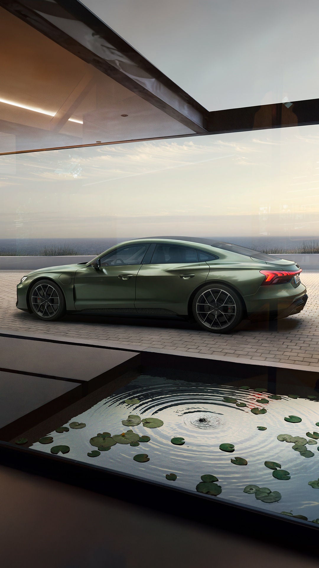 Seitenansicht eines metallic-grünen Audi RS e-tron GT performance vor großer Glasfront, im Vordergrund ein Wasserbecken mit Seerosen.