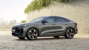Der Q6 Sportback e-tron steht schräg seitlich vor einer begrünten Steinwand. Im Hintergrund ist die Skyline einer Stadt zu erkennen.