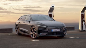 An electric Audi at a charging station with a sunset and mountains in the background.