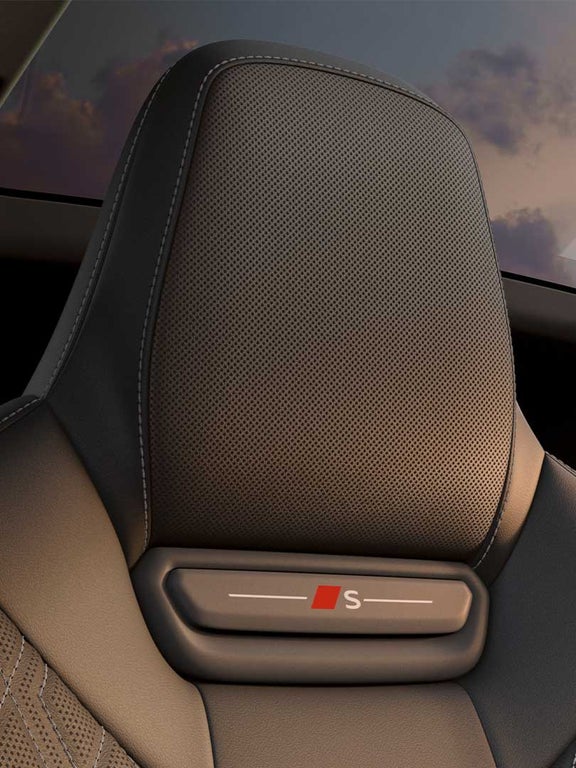 Kopfstütze eines schwarzen Ledersitzes unter einem Panorama-Glasdach bei Sonnenuntergang.