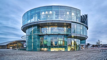 Glass building with several floors in daylight, large window fronts and visible interior.