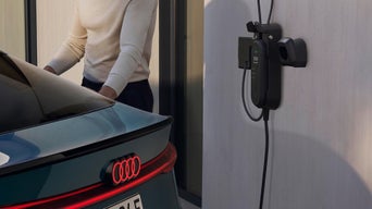 A man connects an Audi electric vehicle to a sleek wall-mounted charger, showcasing modern electric car charging technology.