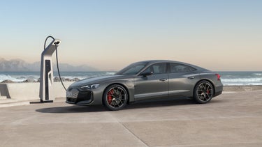 Ein grauer Audi RS e-tron GT lädt an einer Ladestation an der Küste mit Wellen und Bergen im Hintergrund.