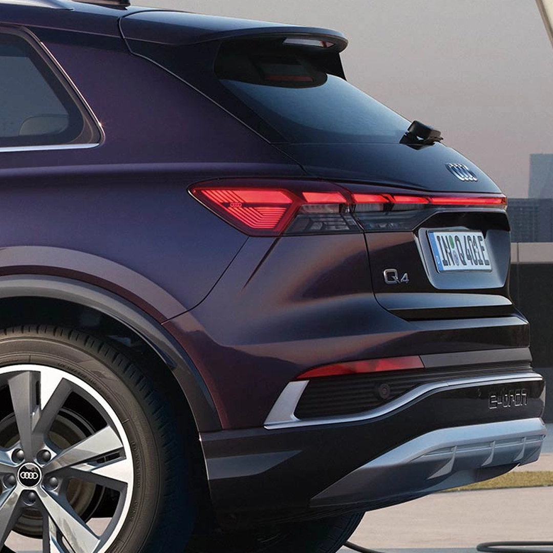 Dark purple Audi Q4 e-tron with rear quarter visible, showing red taillights, silver rim, and 'e-tron' badge.