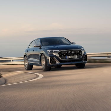 Ein dunkelblauer Audi SQ8 SUV fährt auf kurviger Straße mit leichter Neigung.