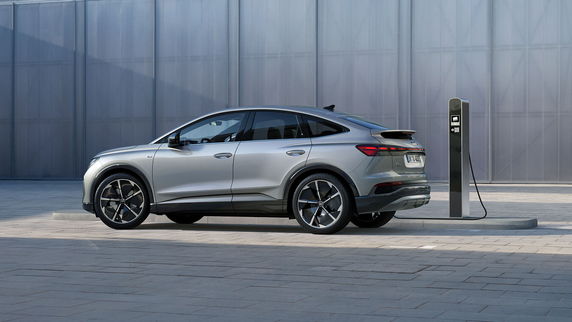 Ein silberner Audi Q4 e-tron an einer Ladesäule vor einer grauen Mauer