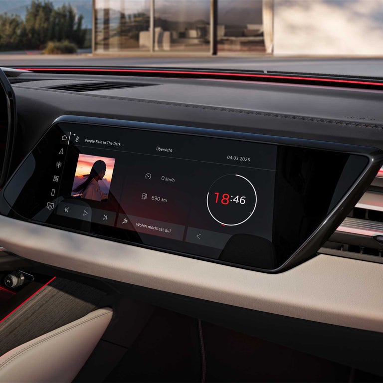 Zentraldisplay eines Audi A6 Avant zeigt Musiktitel, Geschwindigkeit, Reichweite von 690 km und digitale Uhrzeit 18:46.