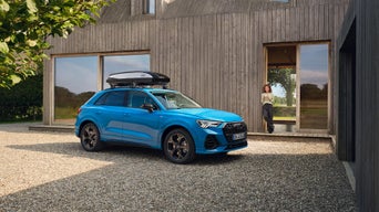 Audi mit Dachbox vor Haus mit Frau