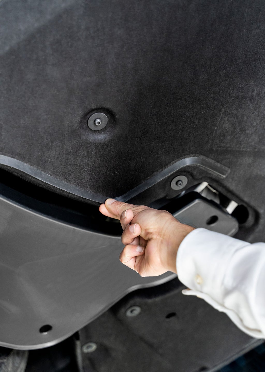 En hånd peker på en plaststripe på undersiden av bilen. 