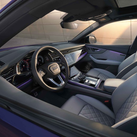 Innenraum eines Audi Q8 SUV in velvet lila mit weißen Leder-Sportsitzen, großem Touchdisplay, Lenkrad und digitalem Cockpit.