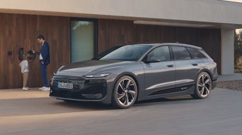 Der A6 Avant e-tron steht seitlich vor einem modernen Haus. An der Hauswand ist eine Ladestation montiert, an welcher ein Vater mit seinem Kind steht.