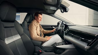 Mann sitzt lächelnd auf dem Fahrersitz eines Audi Modell und legt die Hand auf das Lenkrad im exklusiv anmutenden Innenraum.