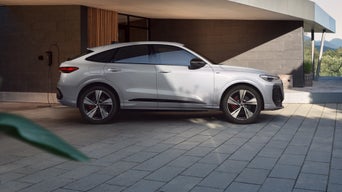 Una Q5 Sportback e-hybrid bianca si trova di fronte a un edificio moderno.