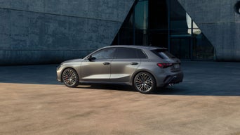 Grauer Audi A3 Sportback vor modernem Betongebäude bei Tageslicht.