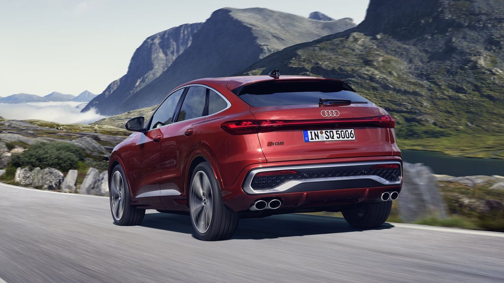 Schräges, hinteres Seitenprofil des roten SQ5 Sportback, welcher auf einer Straße durch die Berge fährt.