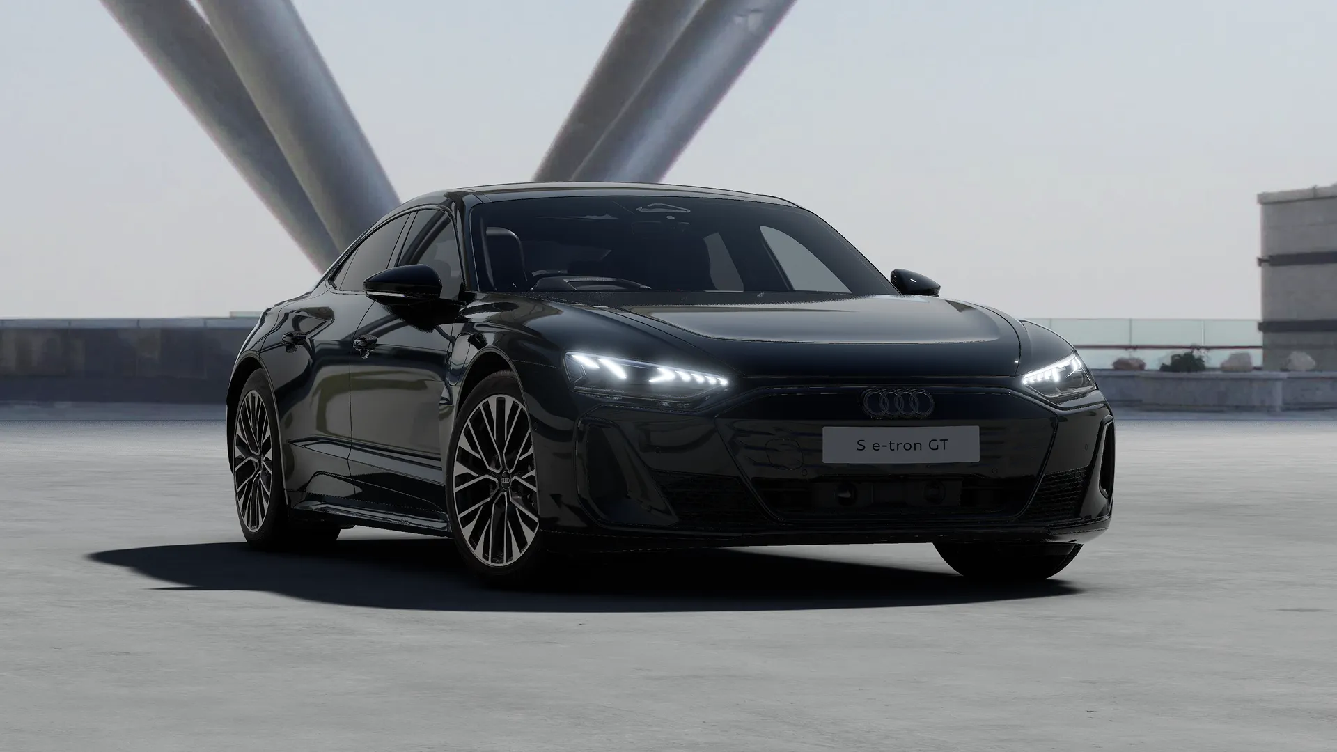 Black Audi S e-tron GT parked on a driveway in front of a modern building with a view.