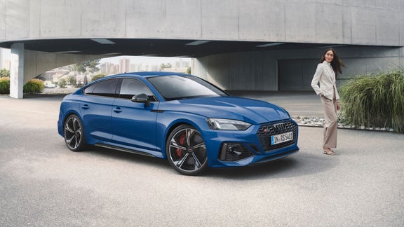 A blue sedan parked under a bridge with a person standing nearby.