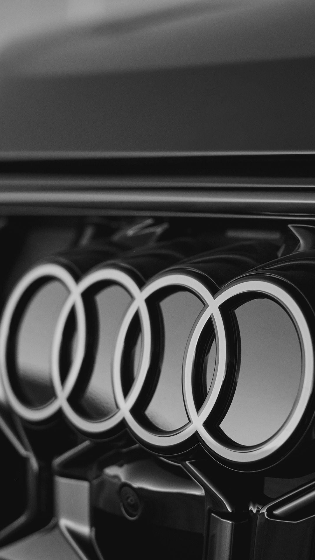 Close-up black and white image of Audi’s four-ring logo on the vehicle’s front grille.