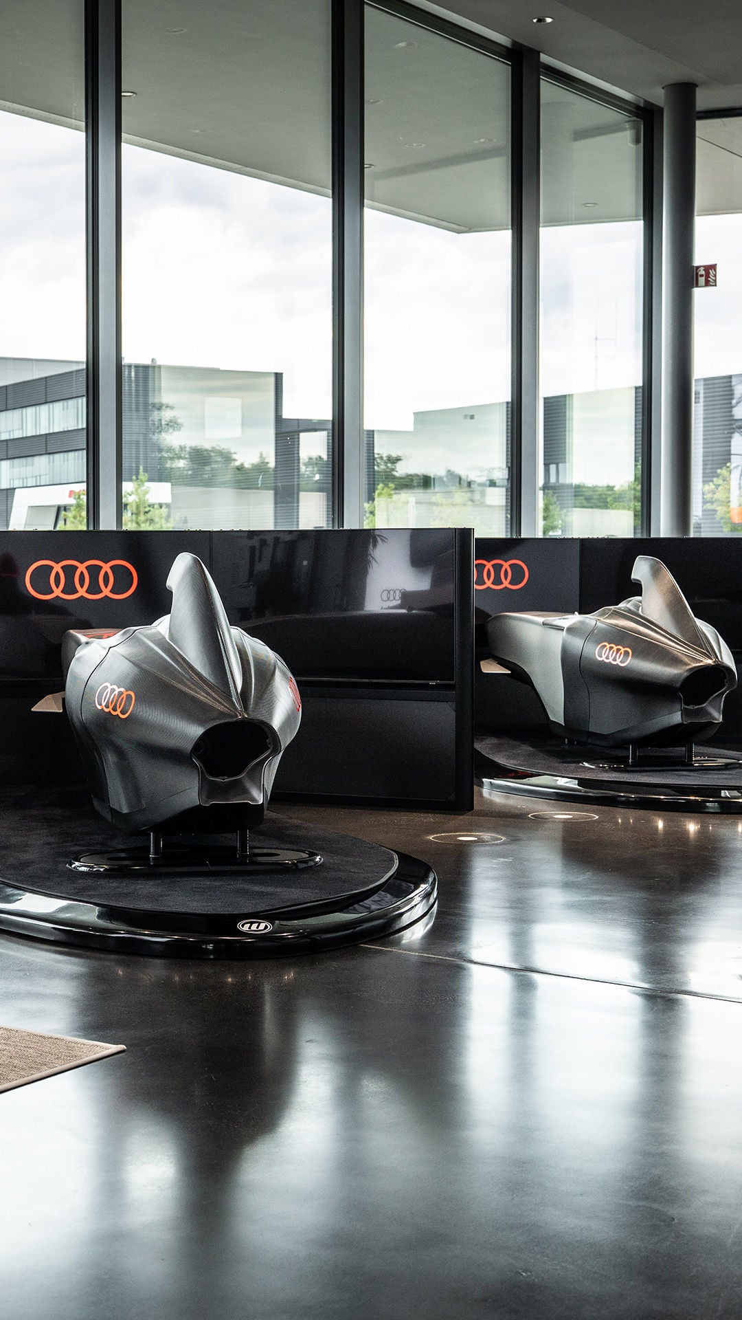 Drei Audi racing Simulator stehen nebeneinander im Showroom; links zeigt ein Bildschirm Zeiten und Rangliste.