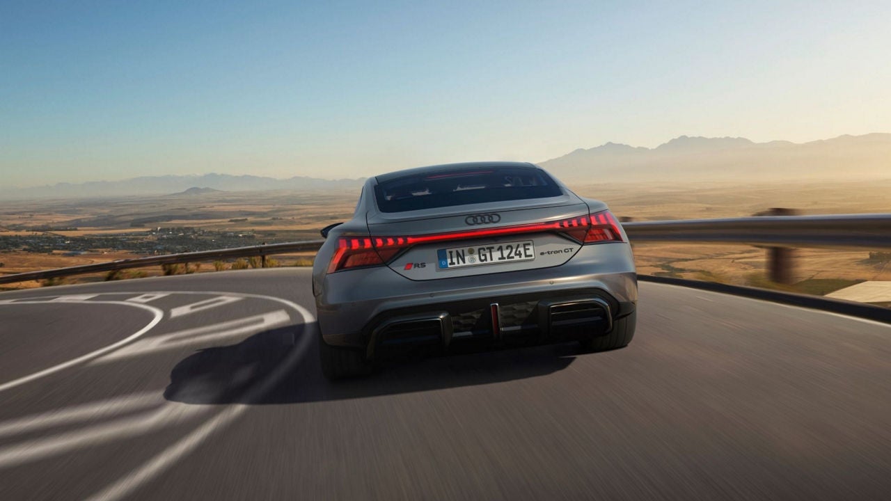 A grey Audi RS e-tron GT driving on a mountain road with a scenic backdrop.