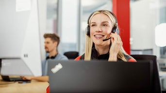 Young man smiles and sits at his workstation at the Mac and writes something on the keyboard, he wears headphones with cables in his ears