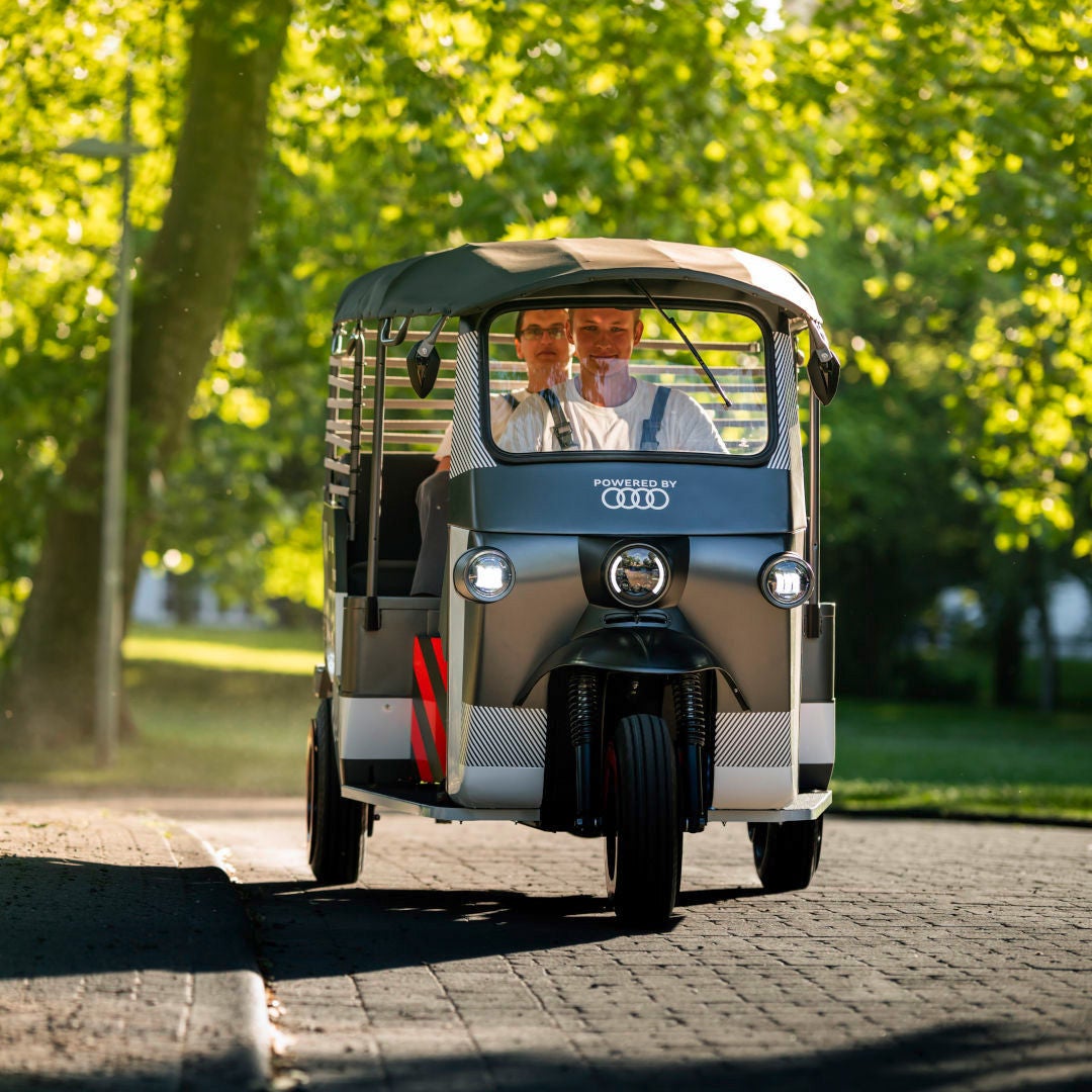 An e-rickshaw drives along a cobbled road lined with trees.