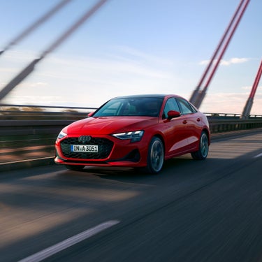 Rote Audi A3 Limousine fährt auf einer Brücke bei Tageslicht, aufgenommen aus schräger Frontansicht.