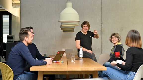 Dani, Ambassador SDC, is talking to her colleagues and sitting on a table