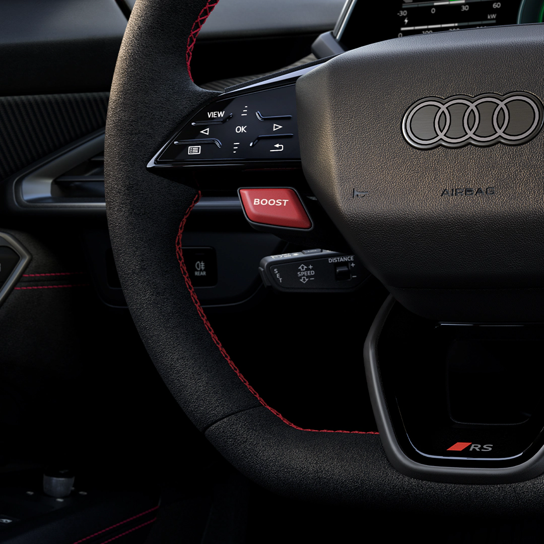 Black steering wheel with red stitching and Audi logo, featuring buttons including a red "BOOST" button.