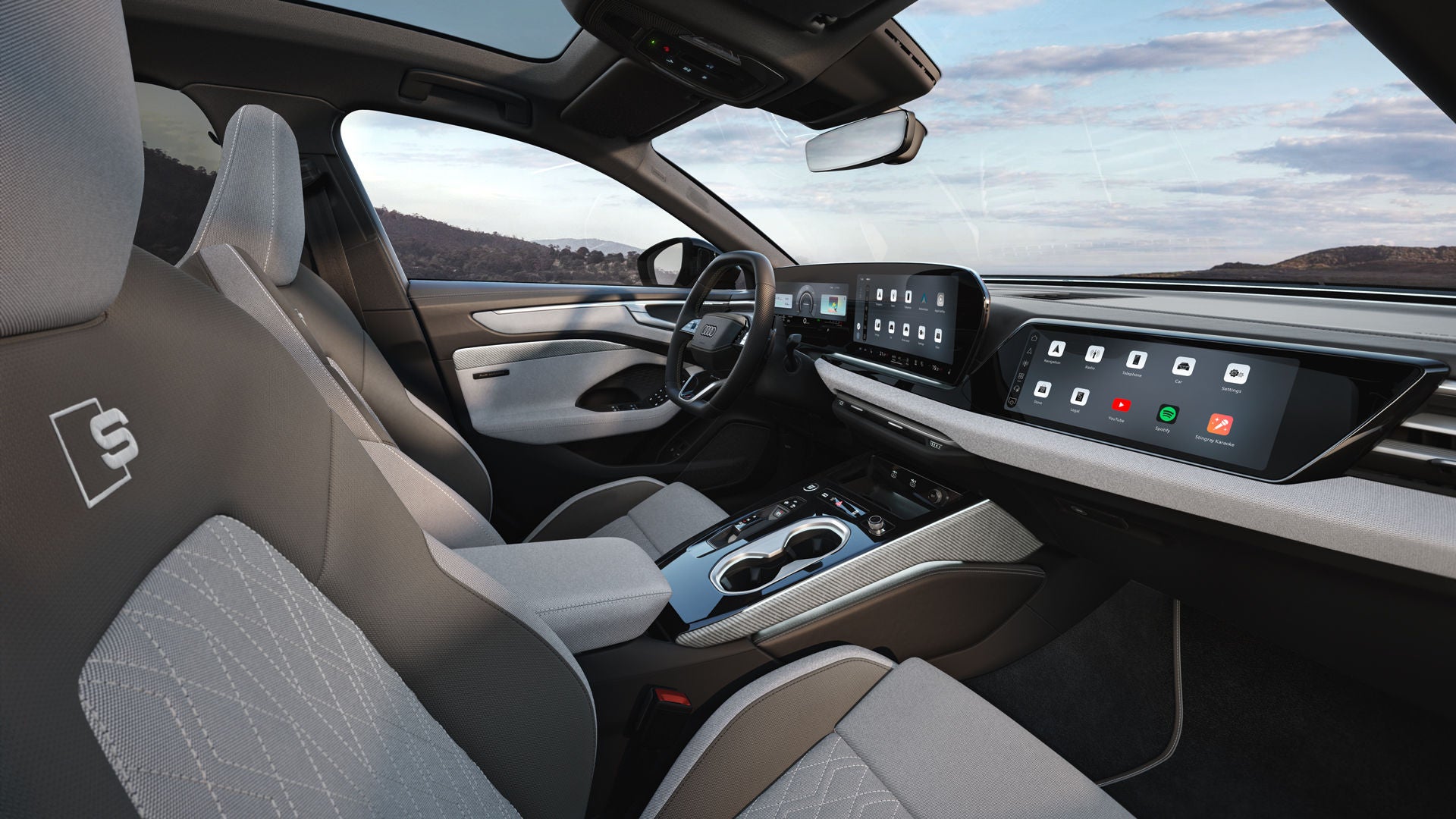 The interior of the A6 Saloon e-hybrid viewed from the front passenger-side B-pillar. The focus is on the sports seats in light gray/neodymium gold fabric, featuring light gray linen-weave decorative inlays.