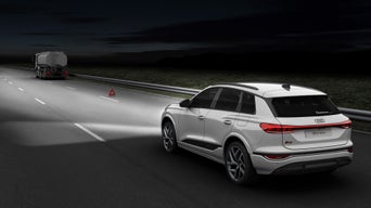 An Audi drives along a dark road at night, where a lorry with a warning triangle is parked on the hard shoulder.