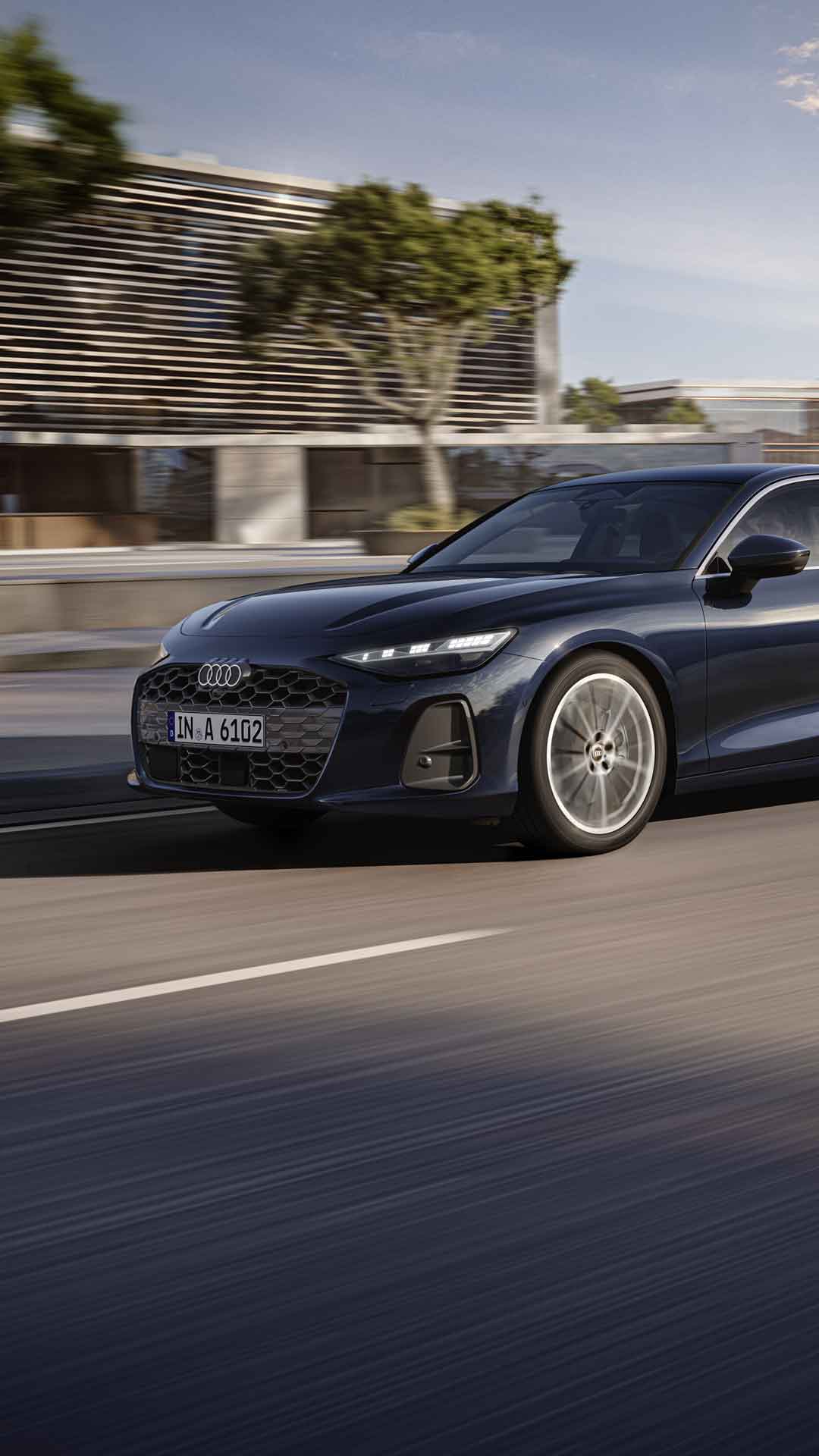 Die A6 Limousine fährt im schrägen Frontprofil auf einer Straße in der Innenstadt.