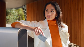 Eine Frau lehnt an einer Ladesäule mit der Tankkarte in der Hand