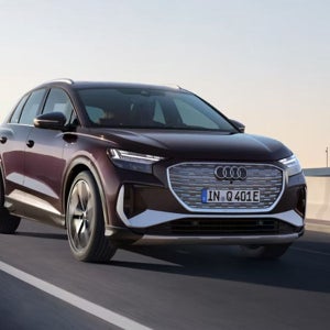 A maroon Audi SUV driving on an open highway at sunset. The car's modern design and dynamic motion convey elegance and innovation.