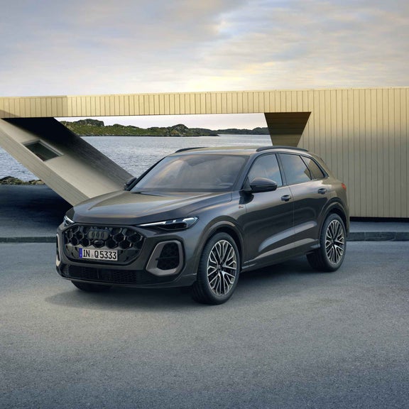 Der Q5 SUV in der edition one mit Kontrasten in Magnesiumgrau steht im seitlichen Frontprofil auf einem Parkplatz direkt an der Küste. Dahinter ein futuristisches Haus.