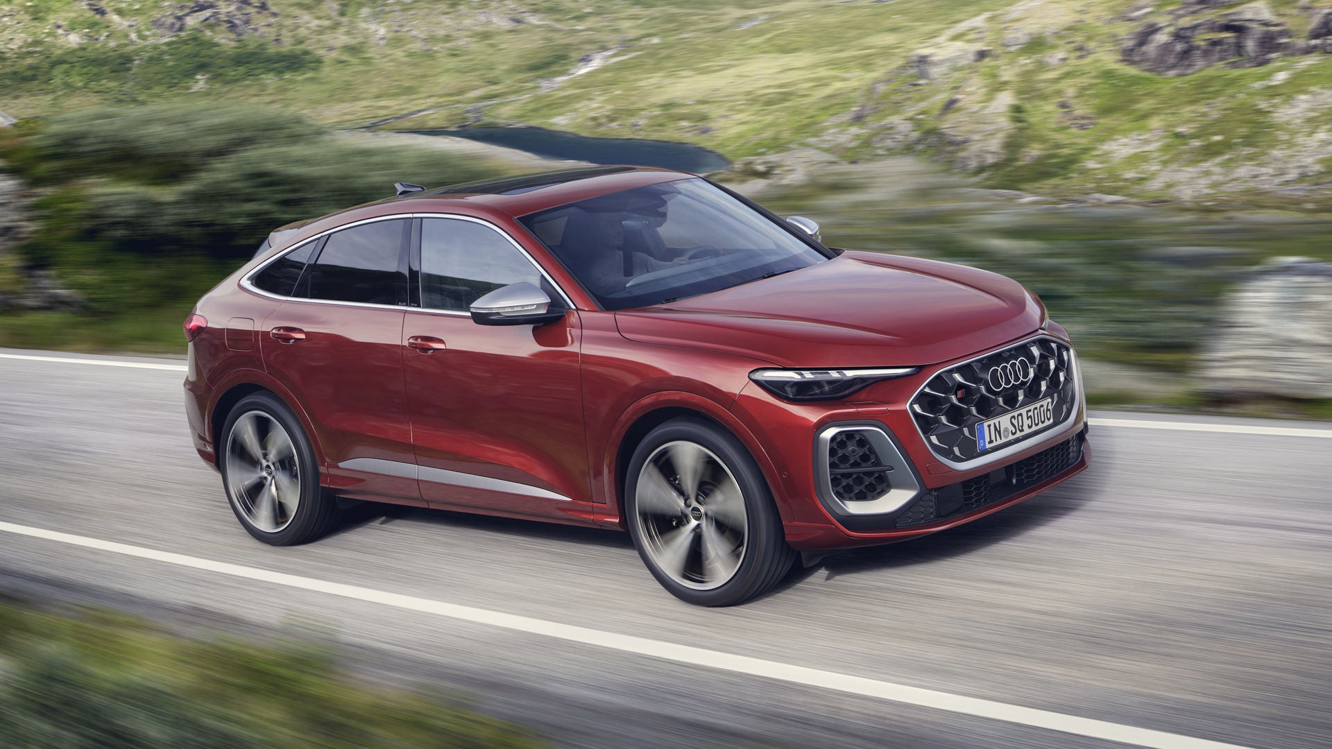 Der rote SQ5 Sportback fährt über eine Straße in den Bergen. Ein junger Mann sitzt am Steuer.