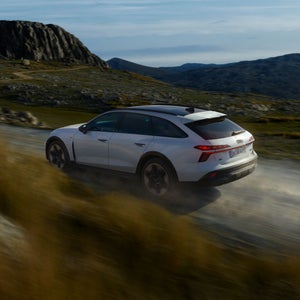 Audi A6 allroad e-hybrid, sedd från sidan när den susar fram längs en bergsväg.
