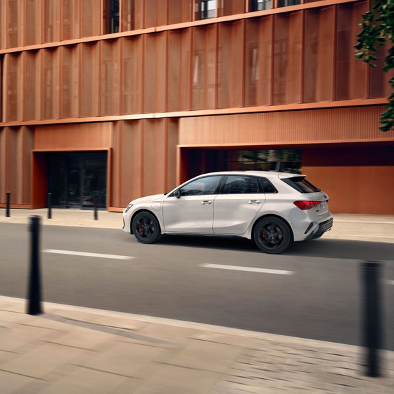 White hatchback car in motion on urban road, modern building backdrop.