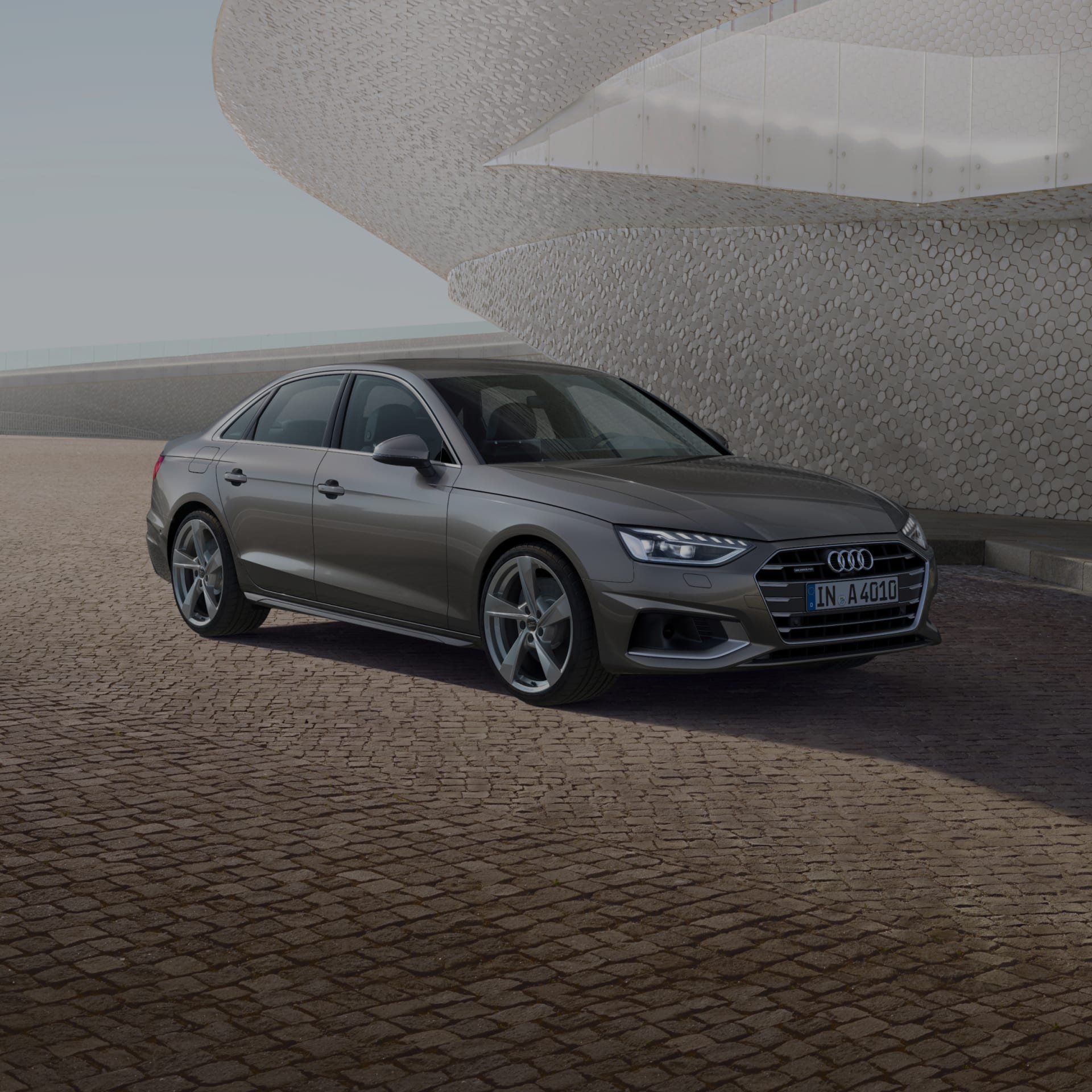 A grey Audi sedan parked near a unique textured building under a clear sky.