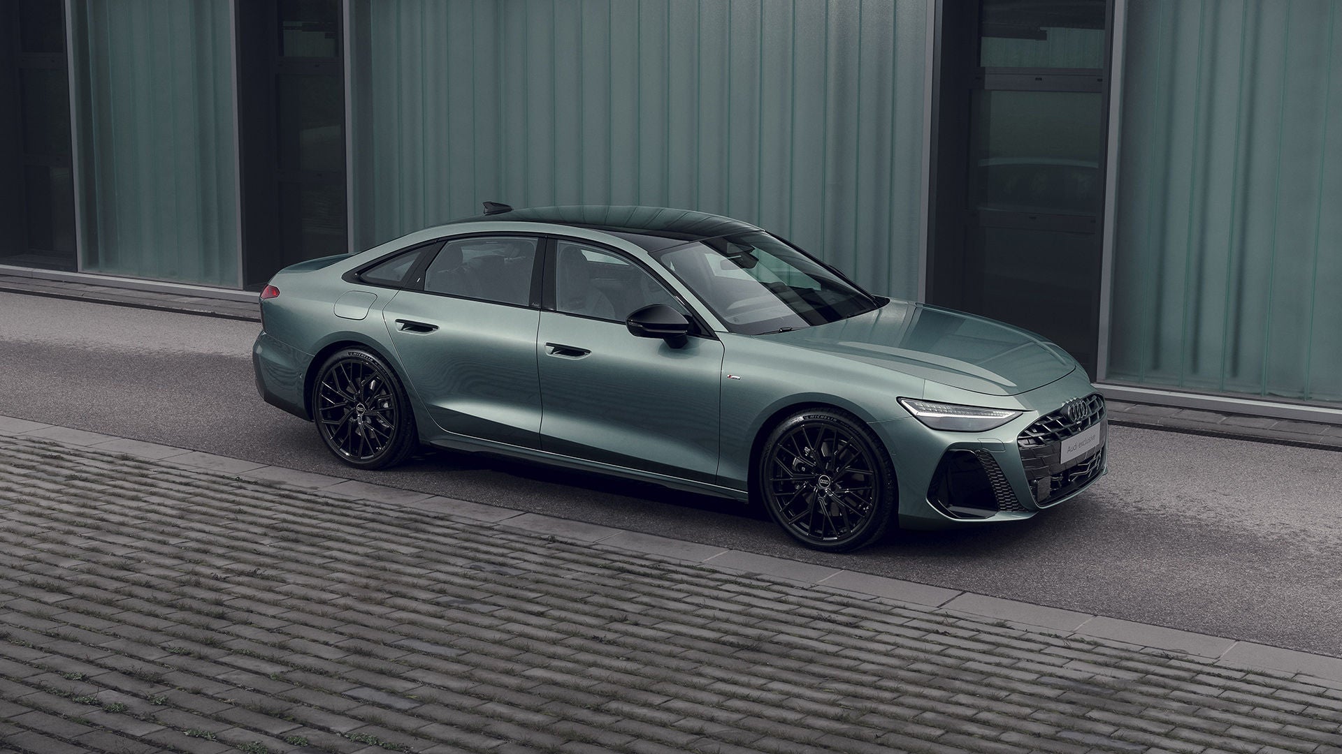  Audi A6 Sedan in Morning Dew Green pearl effect Audi exclusive side view in front of a modern building, black rims, and panoramic roof.